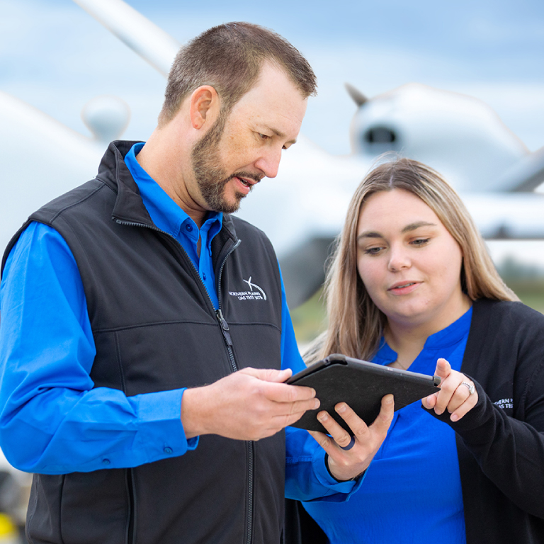 Two people in branded NPUASTS clothing looking at a tablet