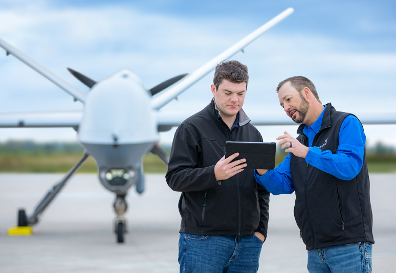 Two men in front of a large unmanned vehicle are looking at a small tablet