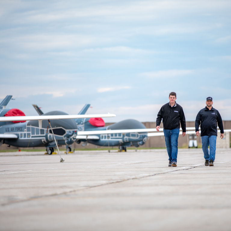 Two men walking away from large unmanned vehicles in the distance