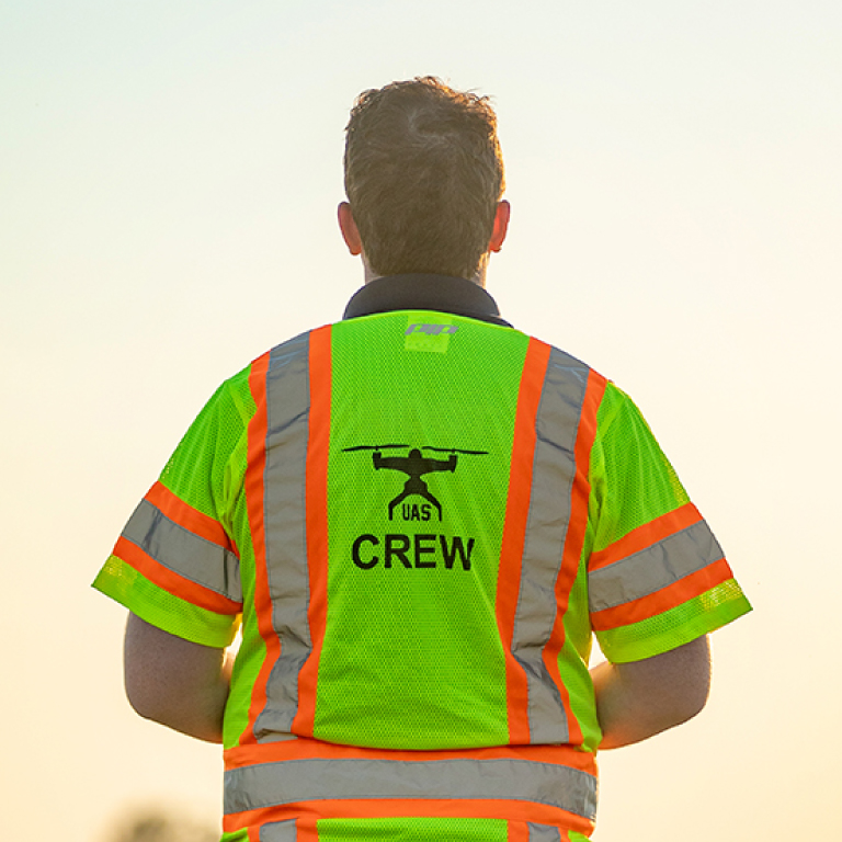 A man wearing a high-visibility shirt with the words"UAS CREW"