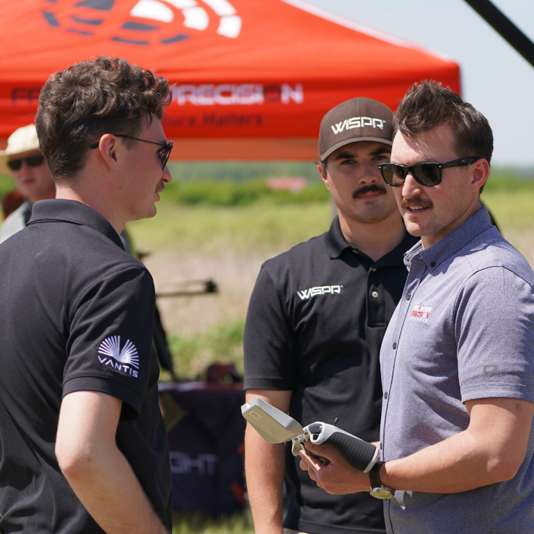 A men with a controller, and two others, stand near a red tent