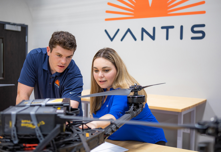 Two people inspecting a small unmanned vehicle on a table